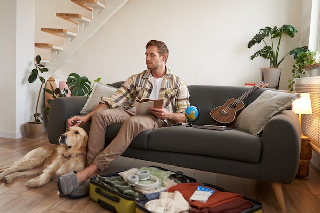 Bezpłatne zdjęcie portret mężczyzny siedzącego z psem pakującego walizkę na wakacje w wycieczce z zwierzęciem