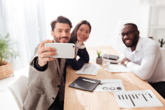 Portret międzynarodowych biznesmenów i bizneswoman siedzących przy stole i robiących zdjęcia na telefonie komórkowym podczas wspólnej pracy w biurze na białym tle