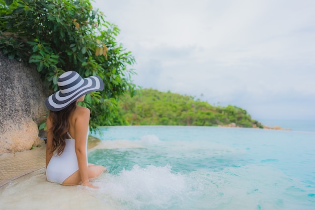 Bezpłatne zdjęcie portret młoda azjatykcia kobieta relaksuje uśmiech szczęśliwego wokoło plenerowego pływackiego basenu w hotelowym kurorcie z dennym widok na ocean