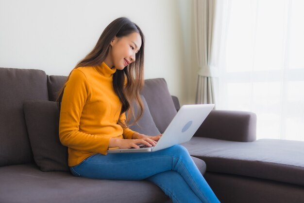 Portret młoda azjatykcia kobieta używa laptop nutową książkę na kanapie