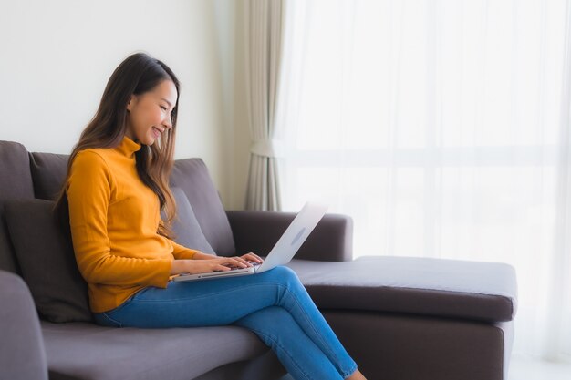 Portret młoda azjatykcia kobieta używa laptop nutową książkę na kanapie