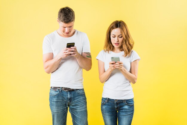 Portret młoda para texting na mądrze telefonie przeciw żółtemu tłu