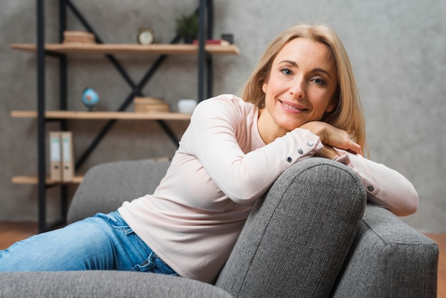 Portret młoda uśmiechnięta kobieta opiera na kanapie w domu