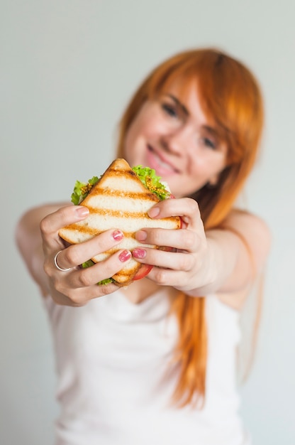 Bezpłatne zdjęcie portret młoda uśmiechnięta kobieta pokazuje piec na grillu kanapkę przeciw białemu tłu