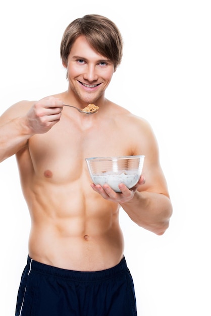 Portret młodego atrakcyjnego mężczyzny mięśni jedzenie płatki z mlekiem - na białym tle na białej ścianie.