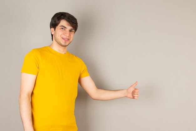 Portret młodego człowieka stojącego i pokazującego kciuk przeciwko szarości.