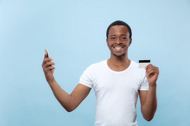 portret młodego mężczyzny afro-amerykańskiego w białej koszuli, trzymając kartę i smartfon.