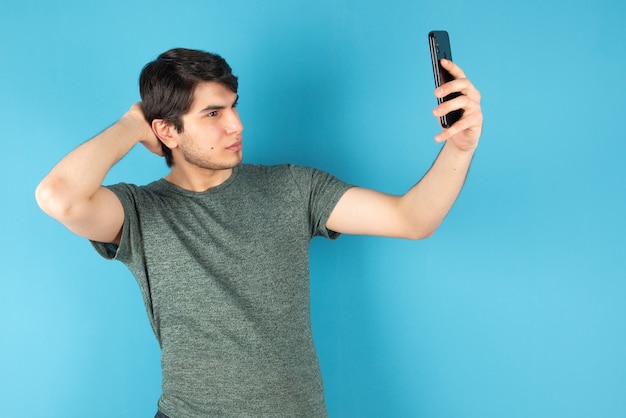Portret młodego mężczyzny biorąc selfie z telefonu komórkowego na niebiesko.