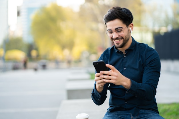 Portret młodego mężczyzny korzystającego z telefonu komórkowego, stojąc na zewnątrz