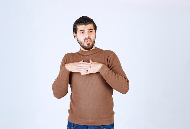 Portret młodego mężczyzny model stojący i trzymający się za ręce na klatce piersiowej.