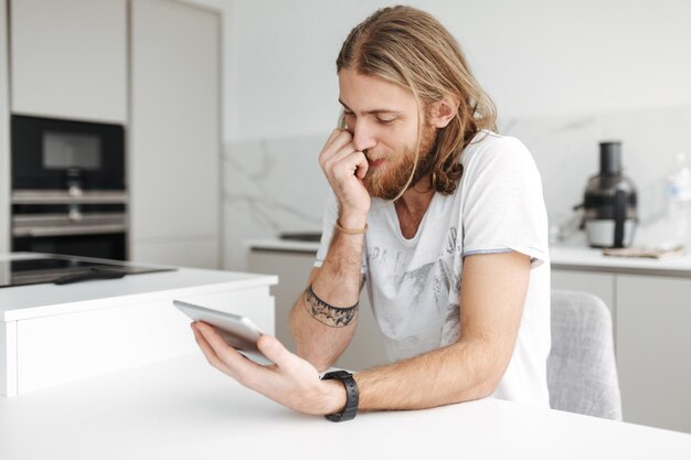 Portret młodego mężczyzny siedzącego z cyfrowym tabletem w ręku w kuchni w domu