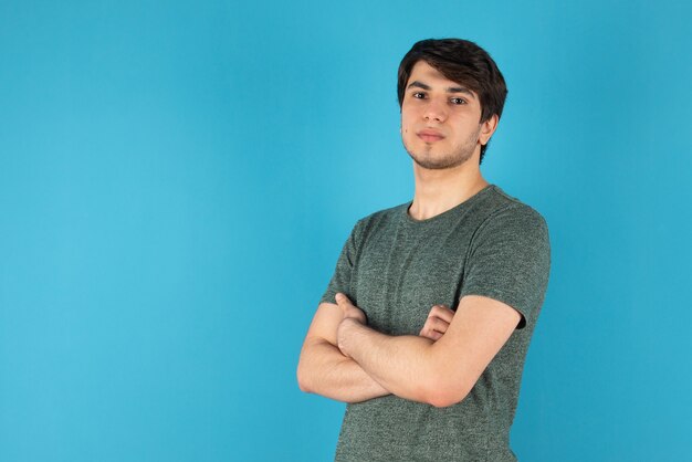 Portret młodego mężczyzny stojącego ze skrzyżowanymi rękami na niebiesko.
