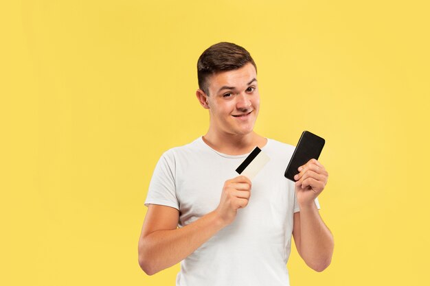Portret młodego mężczyzny, trzymając smartfon i kartę kredytową na białym tle na żółtej ścianie