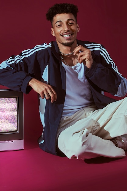 Bezpłatne zdjęcie portret młodego mężczyzny w stylu mody z lat 2000. pozuje z telewizorem