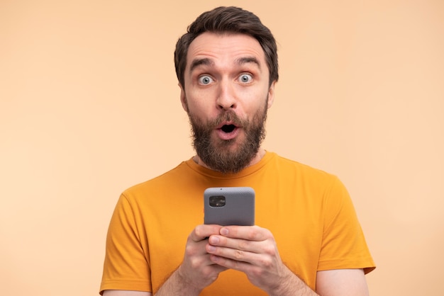Portret młodego mężczyzny w szoku i trzymającego smartfon