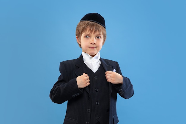 Portret młodego ortodoksyjnego żydowskiego chłopca na białym tle na niebieskim studio