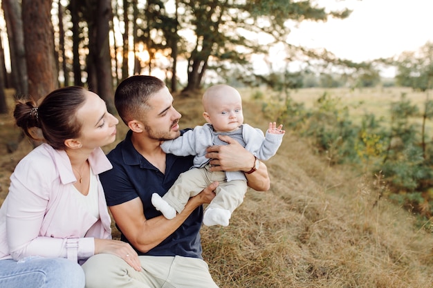 Portret młodej atrakcyjnej rodziny z małym synkiem, pozowanie w pięknym jesiennym lesie sosnowym w słoneczny dzień. Przystojny mężczyzna i jego ładna brunetka żona