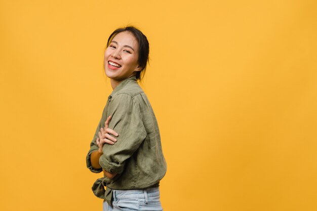 Portret młodej azjatyckiej damy z pozytywnym wyrazem twarzy, skrzyżowanymi rękami, szeroko uśmiechniętym, ubrana w luźne ubranie na żółtej ścianie. Szczęśliwa urocza zadowolona kobieta raduje się sukcesem.