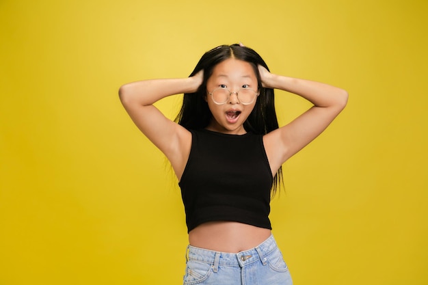 Portret młodej azjatyckiej dziewczyny odizolowanej na żółtym tle studia
