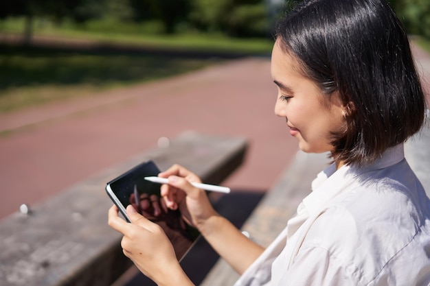 Portret młodej azjatyckiej kobiety rysującej na świeżym powietrzu w parku siedzącej z tabletem graficznym i cyfrowym p