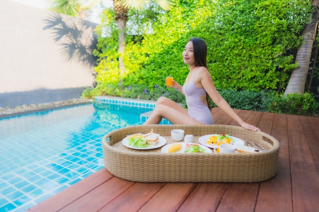 Portret młodej azjatykciej kobiety szczęśliwy uśmiech cieszy się z unosić się śniadaniową tacę w pływackim basenie w hotelu