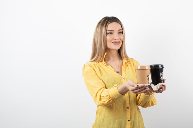 Portret młodej dziewczyny rozdaje filiżanki kawy na białym tle.