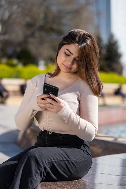 Portret młodej dziewczyny trzymającej telefon i siedzącej w parku Zdjęcie wysokiej jakości