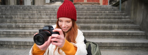 Bezpłatne zdjęcie portret młodej fotografki siedzi na schodach z profesjonalnym aparatem i robi zdjęcia na świeżym powietrzu