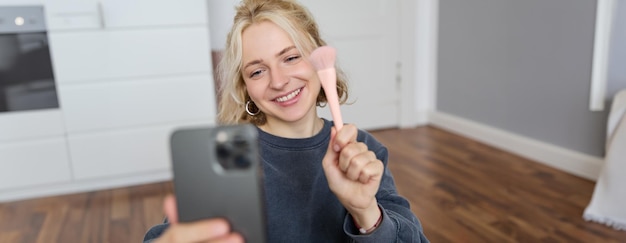 Portret młodej influencerki w mediach społecznościowych robiącej selfie w swoim pokoju, siedzącej na podłodze i trzymającej się za ręce