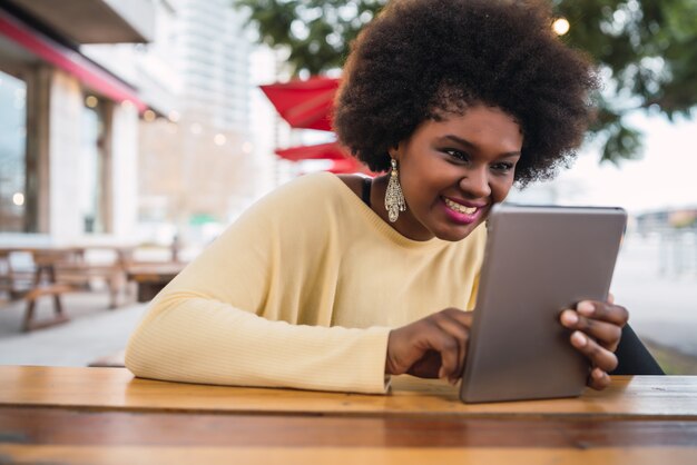 Portret młodej kobiety Łacińskiej afro american przy użyciu jej cyfrowego tabletu, siedząc w kawiarni. Koncepcja technologii.