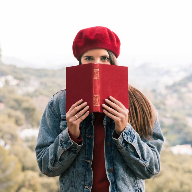 Portret młodej kobiety mienia czerwieni książka przed jej usta przy outdoors