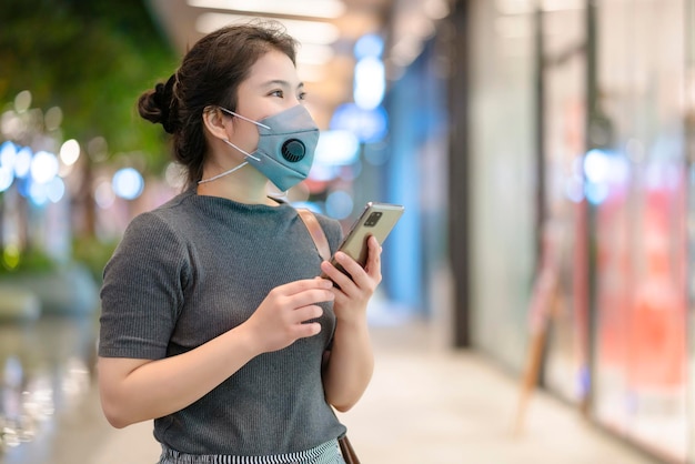 Portret młodej kobiety noszącej maskę ochronną na twarz, aby zapobiec rozprzestrzenianiu się wirusa, ręcznie używać technologii smartfonów, komunikacji, nowej koncepcji normalnego stylu życia