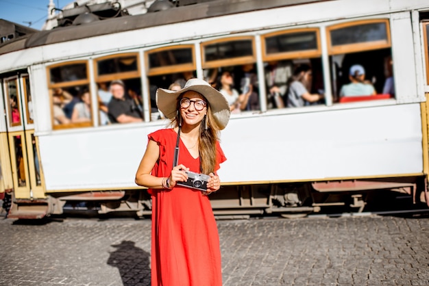 Portret młodej kobiety podróżnika w czerwonej sukience stojącej na ulicy ze słynnym tramwajem turystycznym na tle w lizbonie, portugalia