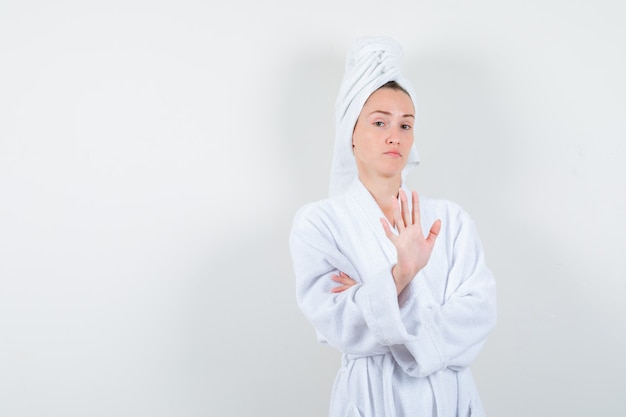 Portret młodej kobiety pokazano gest stop w biały szlafrok, ręcznik i patrząc pewnie z przodu