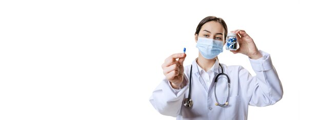 Portret młodej kobiety pracownik medyczny pielęgniarki pokazujący pigułkę na białym tle nad białym studio Koncepcja opieki zdrowotnej