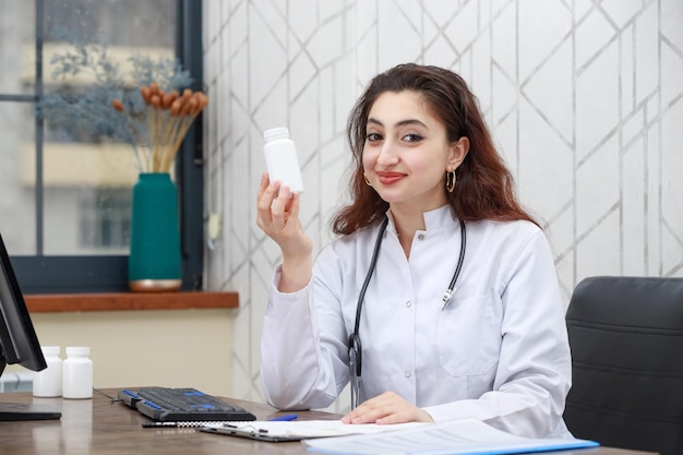 Portret młodej kobiety, pracownika opieki zdrowotnej, trzymającego kapsułkę z lekiem i patrzącego w kamerę Zdjęcie wysokiej jakości