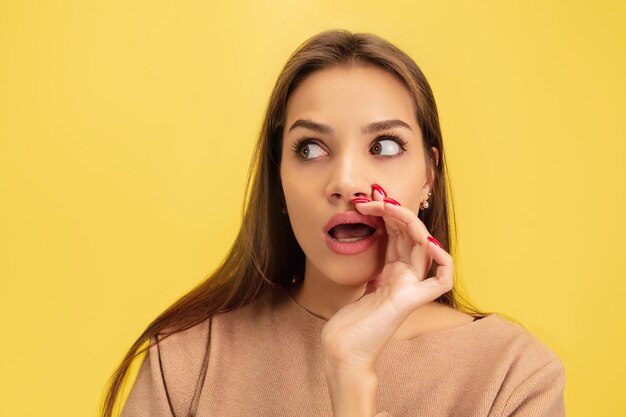 Portret młodej kobiety rasy kaukaskiej z jasnymi emocjami na żółtym studio