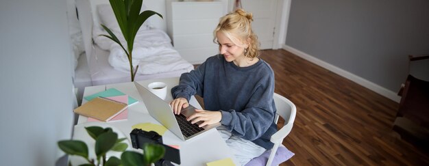 Portret młodej kobiety uczącej się na odległość pracującej w domu z laptopem, robiąc notatki