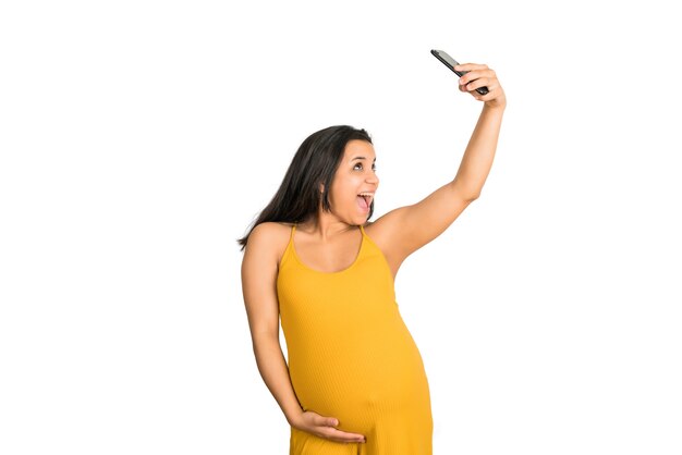 Portret młodej kobiety w ciąży przy selfie z telefonu komórkowego na białym tle. Koncepcja ciąży i macierzyństwa.