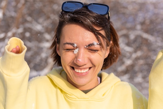Bezpłatne zdjęcie portret młodej kobiety w zimowym lesie w słoneczny dzień ze śnieżnobiałym uśmiechem, wygłupiać się