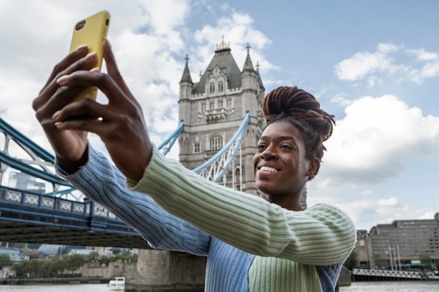 Bezpłatne zdjęcie portret młodej kobiety z dredami afro robi selfie obok mostu w mieście