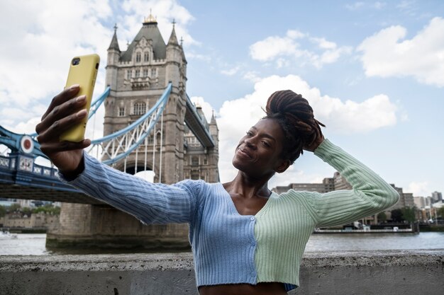 Portret młodej kobiety z dredami afro robi selfie obok mostu w mieście