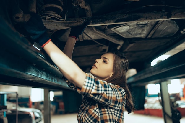 Portret młodej pięknej kobiety pracującej jako mechanik samochodowy naprawiający samochód w salonie samochodowym w pomieszczeniu