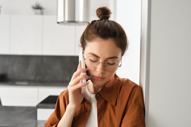 Bezpłatne zdjęcie portret młodej smutnej kobiety w okularach rozmawiającej przez telefon komórkowy i słuchającej wiadomości głosowej