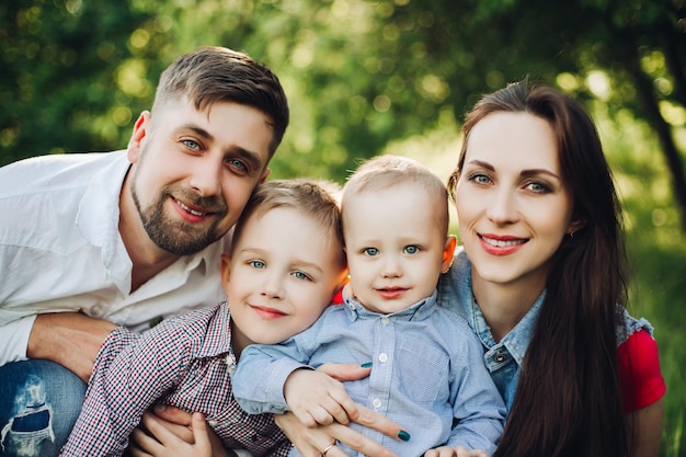 Portret młodej szczęśliwej rodziny, ubrany w zwykłe stroje, spędzający czas razem w parku Mężczyzna i kobieta całuje swoich synków, patrząc i uśmiechając się do kamery