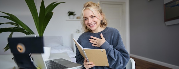 Portret młodej uśmiechniętej blondynki pracującej z domu, rozmawiającej przez internet za pomocą cyfrowej kamery wideo