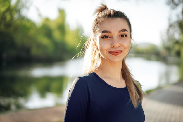 Portret młodej uśmiechniętej kobiety noszącej odzież sportową w porannym parku