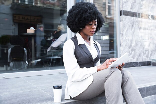 Portret młody afrykański bizneswoman siedzi na zewnątrz biura używać cyfrową pastylkę
