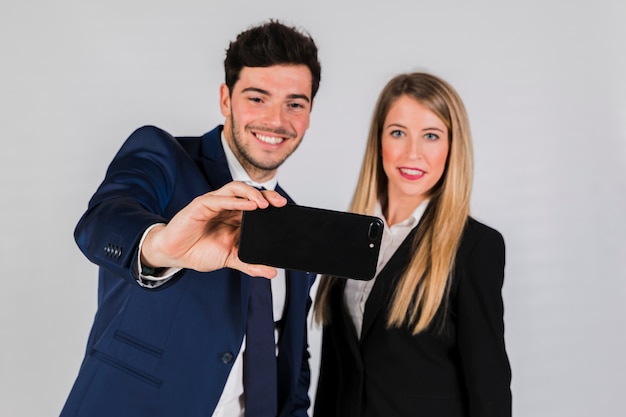 Portret młody biznesmen i bizneswoman bierze selfie na telefonie komórkowym przeciw szaremu tłu