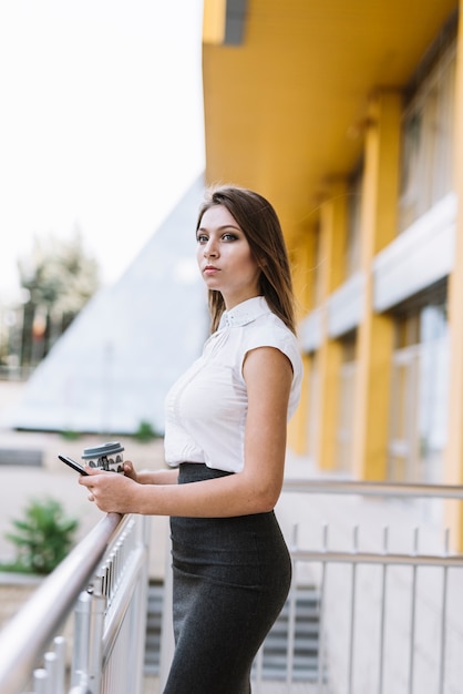 Portret młody biznesmena mienia telefon komórkowy i rozporządzalna filiżanka